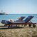 A beachside setup consisting of 2 sunbeds, towels, a hat and a small table with 2 beverages